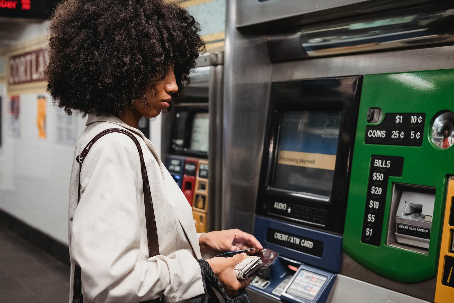 A woman uses a ticket machine in a subway station, handling her wallet and paying for transit.