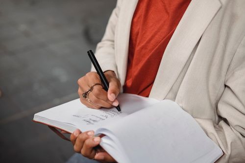 Free Close-up of person writing in notebook outdoors, showcasing casual clothing and thoughtful engagement. Stock Photo