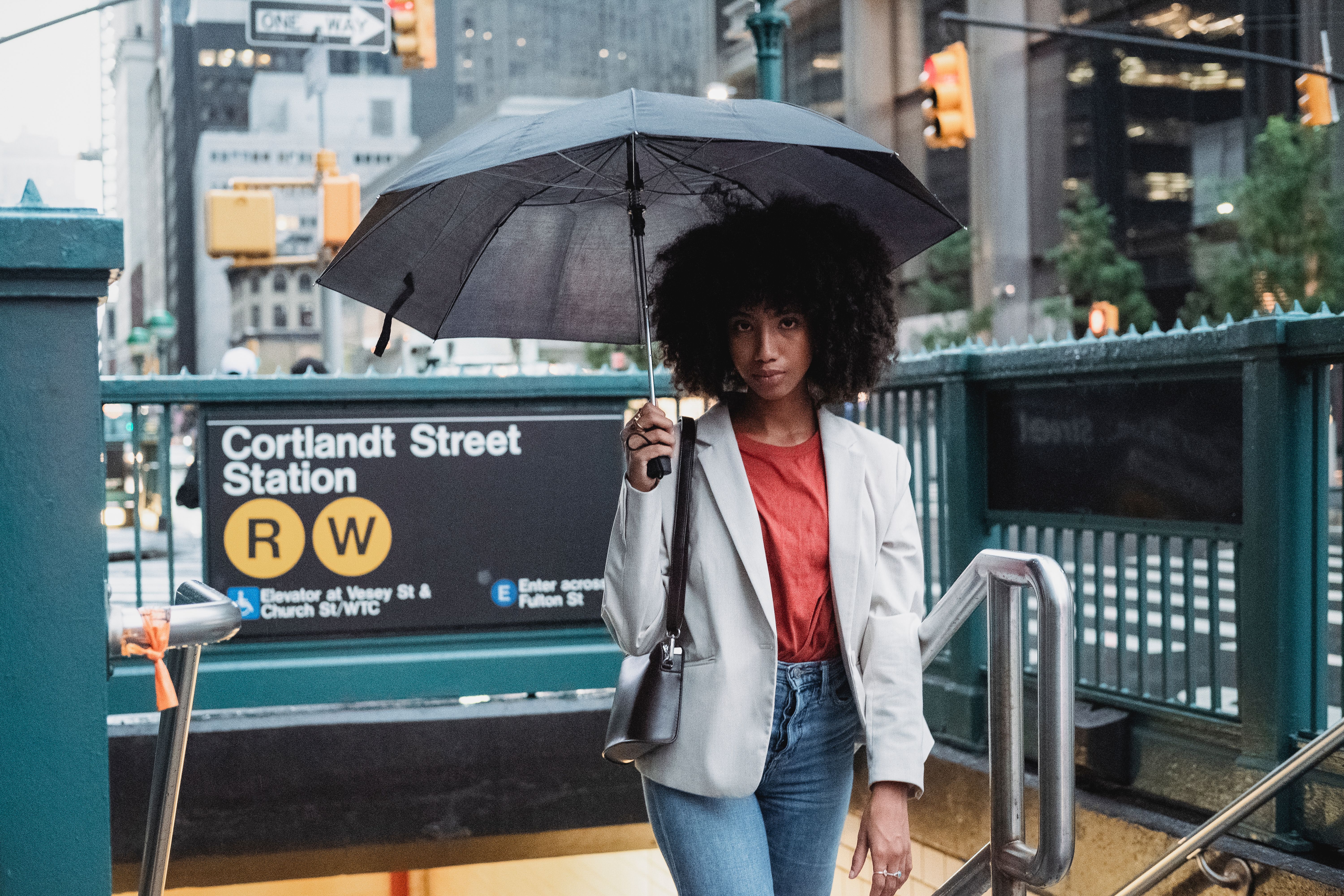 Woman in white blazer holding umbrella at NYC's Cortlandt Street Station entrance.