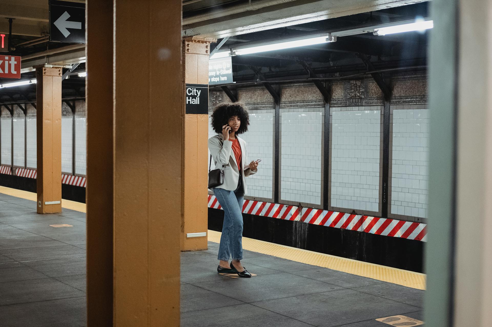 A woman with afro hair making a phone call while waiting at City Hall subway station.