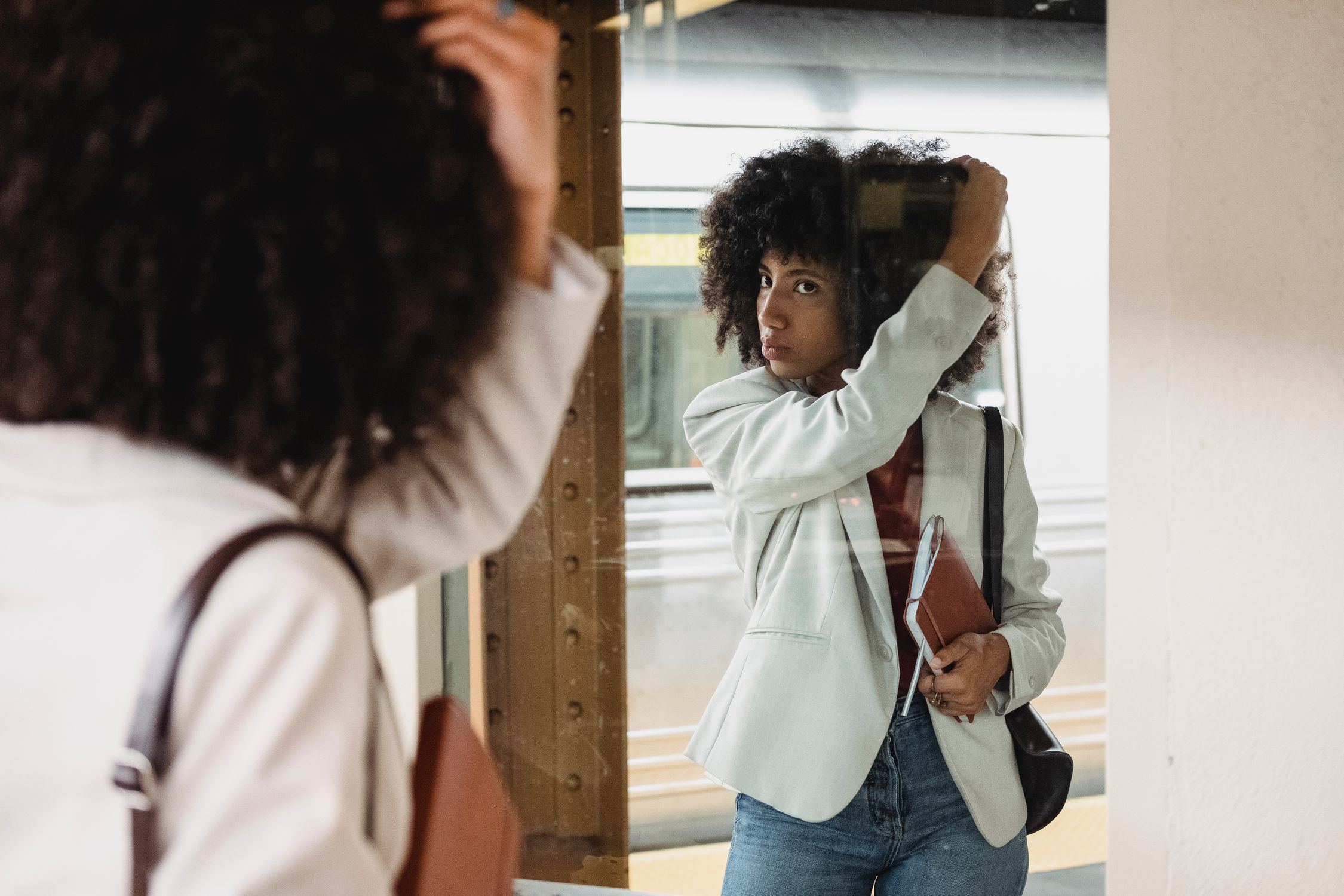 Woman fixing her hair in reflection at subway station. Stylish urban scene.