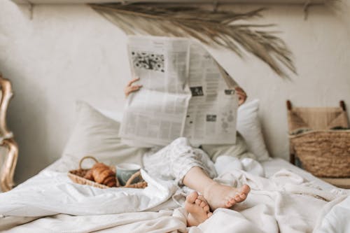 Free Person Sitting on Bed While Reading Newspaper Stock Photo