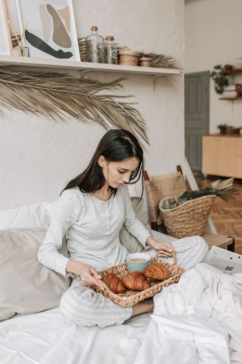 Free Woman having breakfast in bed with coffee and croissants, serene morning scene. Stock Photo