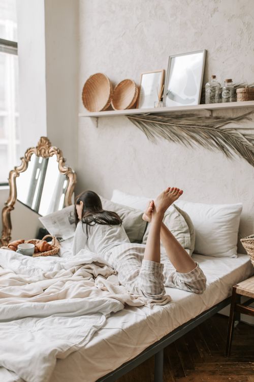 Free A woman lies comfortably on a bed in a stylish bedroom, reading a book with breakfast nearby. Stock Photo