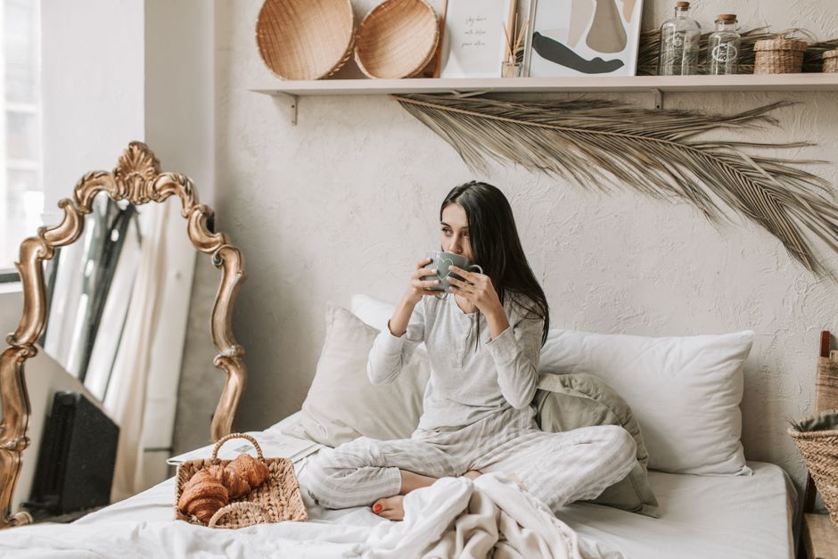 Woman in pajamas enjoys coffee and pastries in a stylish and cozy bedroom setting.
