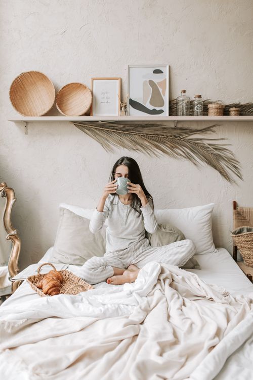 Free Woman enjoying coffee in a stylish bedroom with cozy decor. Stock Photo