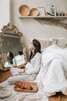 Woman in pajamas enjoying coffee by bed with croissants. Relaxing cozy bedroom vibe.