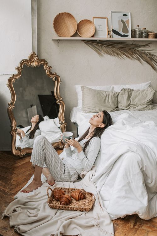 Free A woman enjoys a peaceful morning with a cup of coffee and breakfast in a cozy bedroom setting. Stock Photo