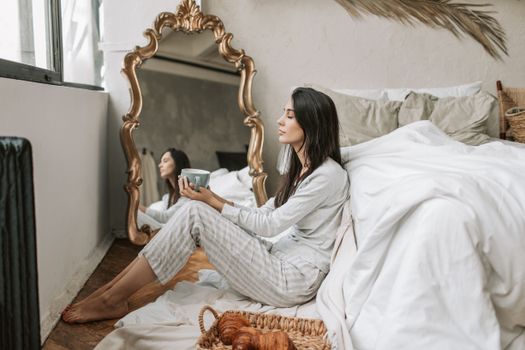 Woman enjoying morning coffee in cozy bedroom setting with elegant decor.
