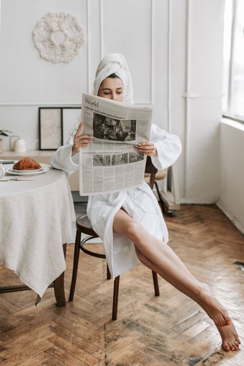 Free Woman in bathrobe reading a newspaper at breakfast in a cozy indoor setting. Stock Photo