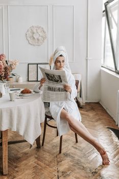 Relaxed woman in bathrobe reading a newspaper in stylish living room setting with natural light.