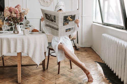 Free Woman in White Robe Sitting on a Chair While Reading Stock Photo