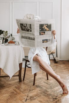 Woman in bathrobe reading newspaper barefooted, enjoying breakfast indoors.