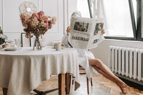 Free Woman enjoying a relaxing morning, reading a newspaper with coffee in a cozy setting. Stock Photo