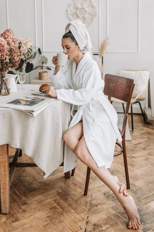 Woman in White Robe Sitting on a Chair while Drinking on a Mug