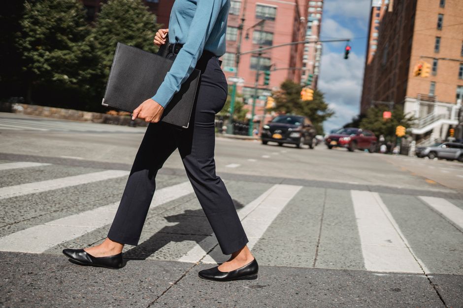 how to create a compelling professional portfolio - Woman in business attire crossing a street in an urban environment with buildings in the background.