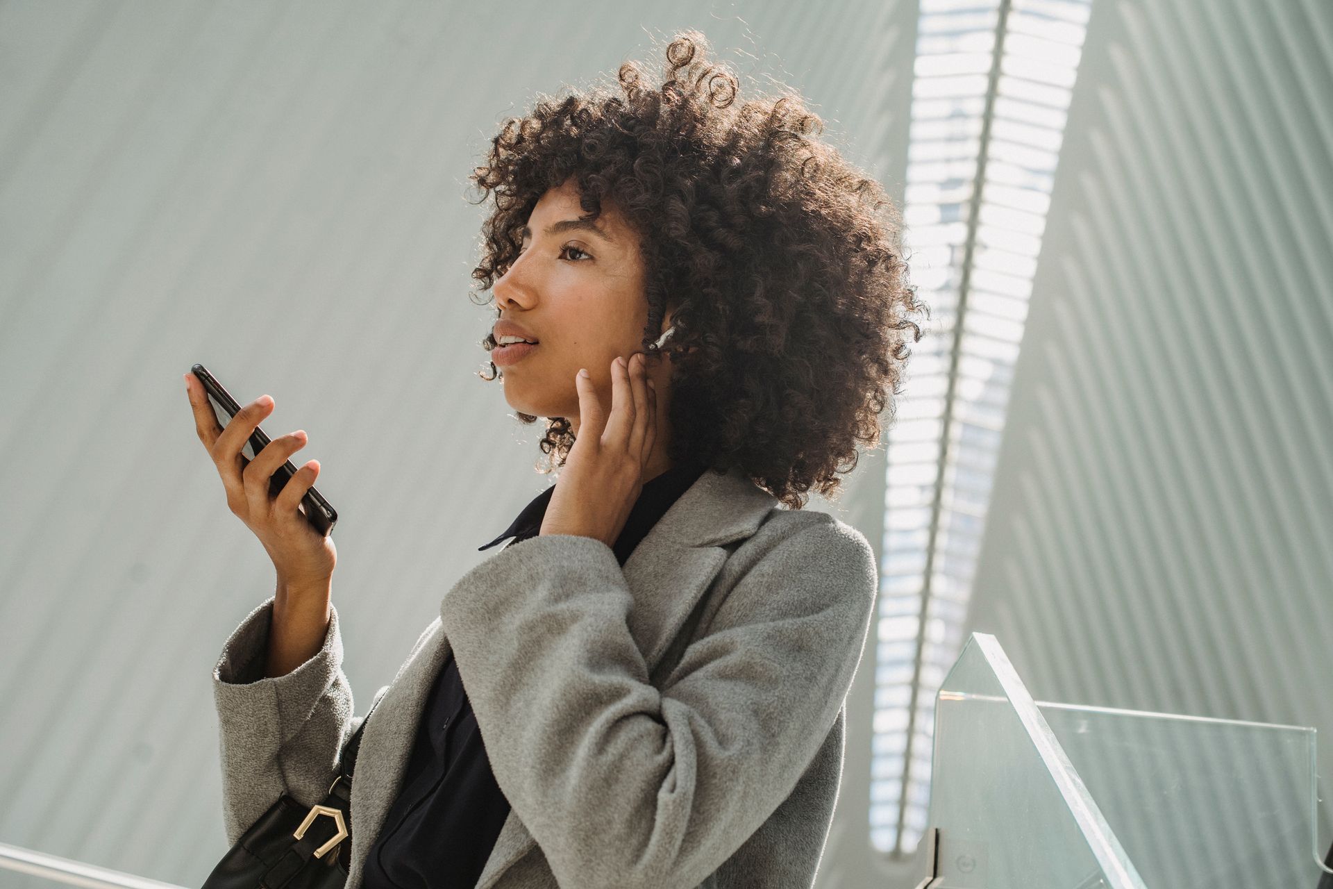 Confident woman using a smartphone and earbud in an urban setting.