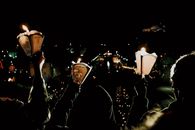 Silhouette of group of people with flaming candles in hands looking at glistening river under black sky at night