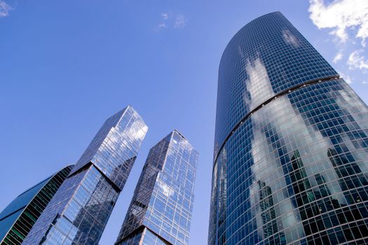 Modern skyscrapers in Moscow with blue glass exteriors and cloud reflections under a clear sky.