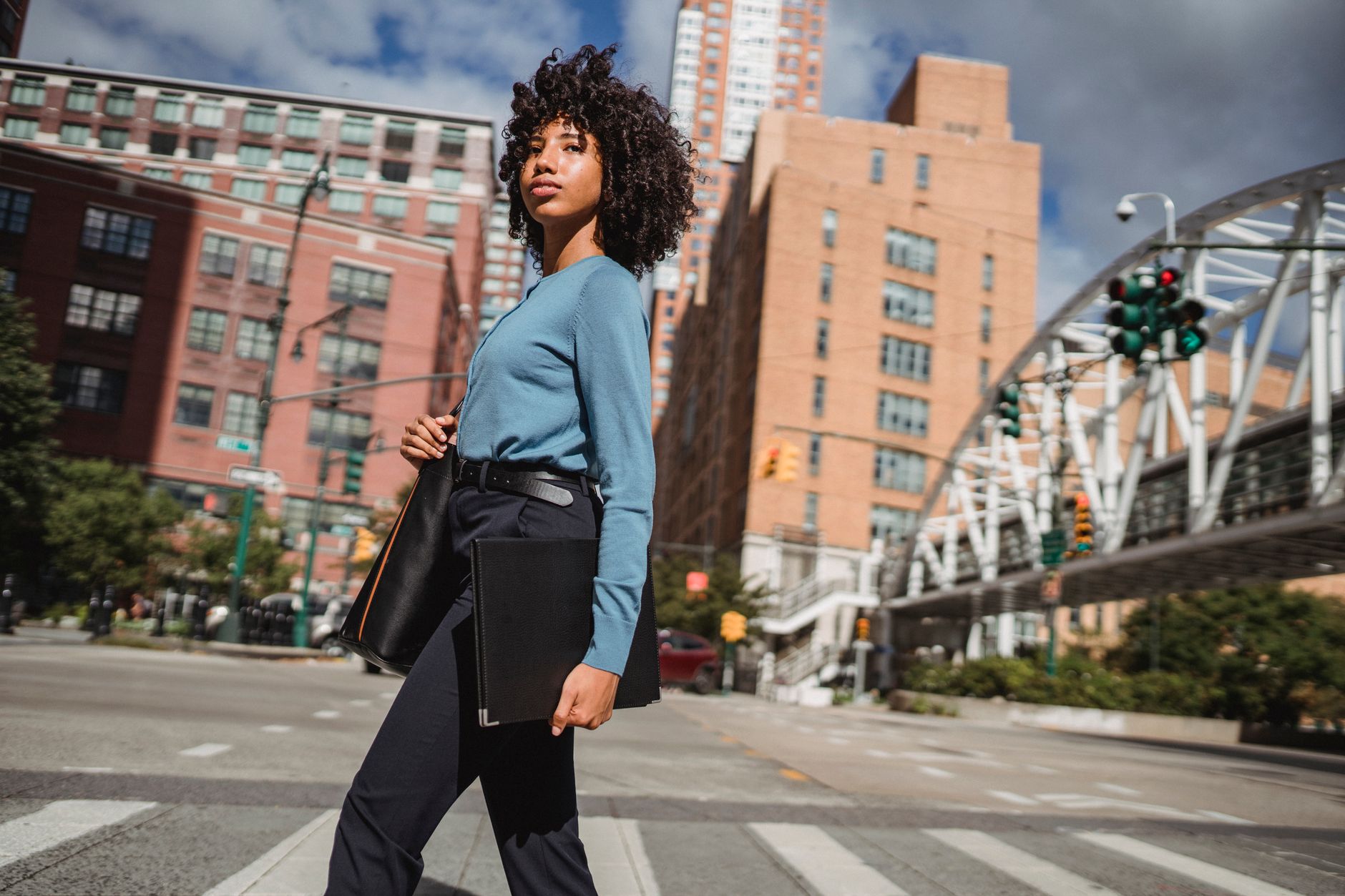 Confident woman walking across a city intersection amidst tall buildings and urban architecture.