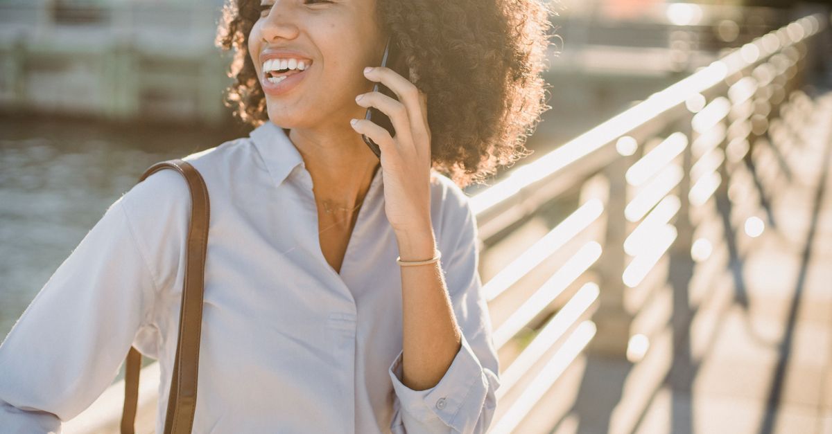 Person walking with a phone in hand, smiling, neighborhood setting