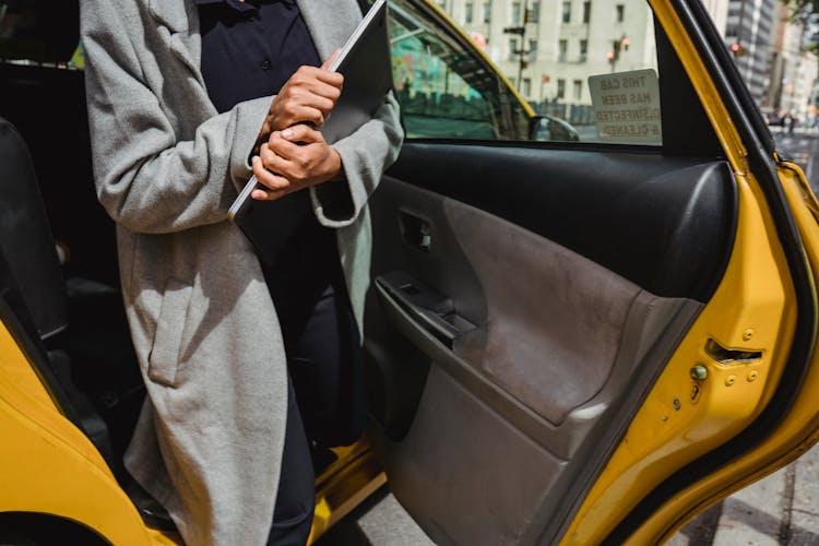 A Person Holding A Laptop While Getting Out Of A Taxi