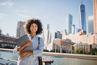 在城市景观中，微笑的女人与笔记本电脑体现了城市的专业精神