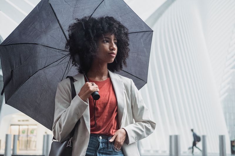 Woman standing under umbrella on a rainy day in an urban setting.