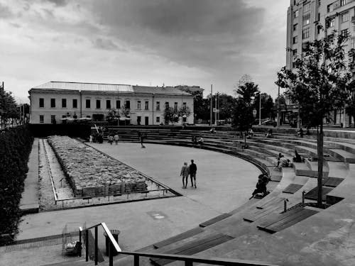Black and white of square located near buildings in city with amphitheater benches forming circular lines and patterns in daytime