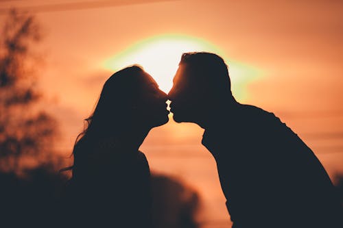 Free Side view of romantic couple standing close and kissing gently under bright sky at sunset Stock Photo