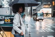一个拿着雨伞的女人站在城市多雨的街道上，靠近地铁入口