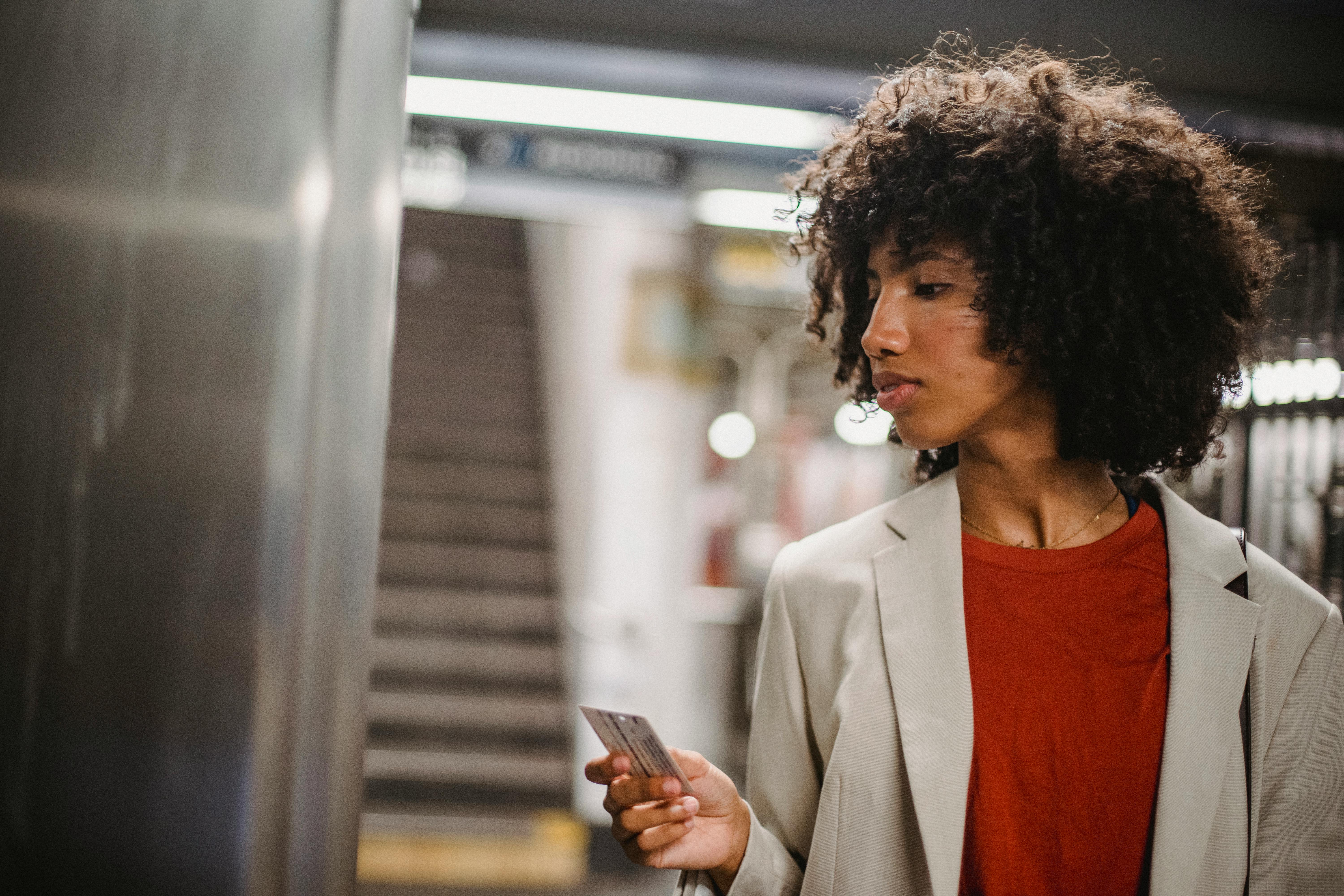 Stylish woman with curly hair using a card in a subway station, wearing a beige blazer.