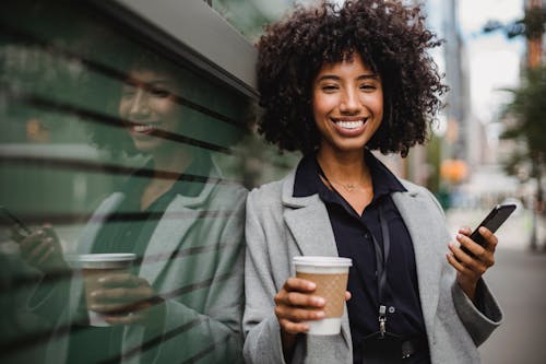 Woman in Gray Blazer Holding White Cup and Black Mobile Phone