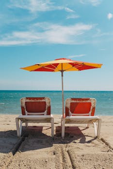 Peaceful seaside scene with empty beach chairs under a colorful umbrella.