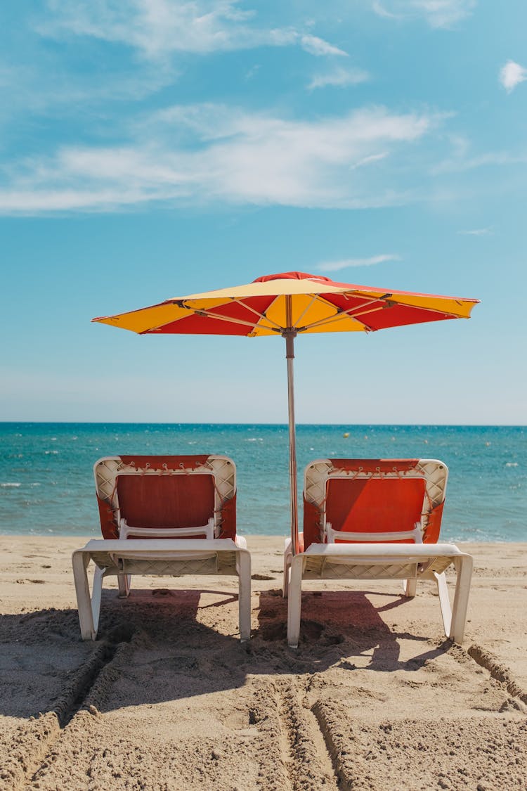 A Beach Umbrella And Beach Chairs Under A Blue Sky