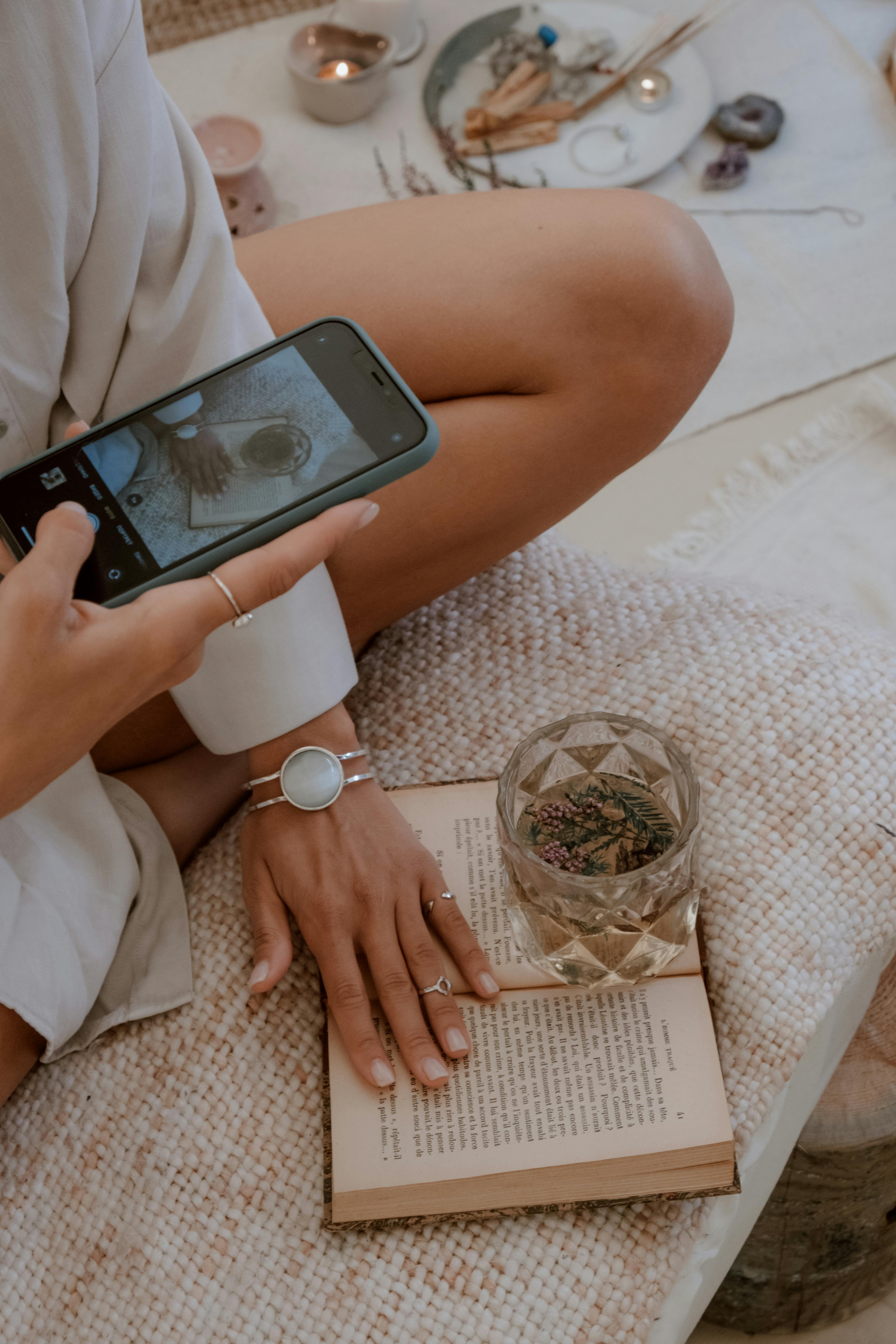 Free Woman taking photo of a relaxing setup with herbal tea and a book. Cozy and serene. Stock Photo