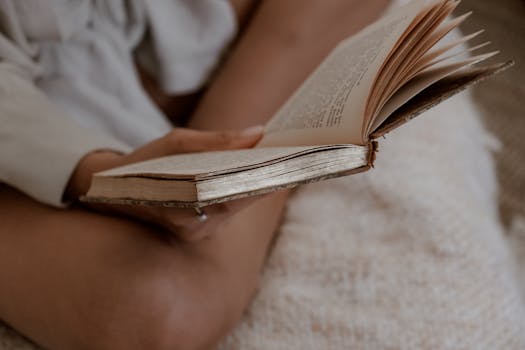 A person relaxing and reading an old, worn-out book in cozy indoor setting.