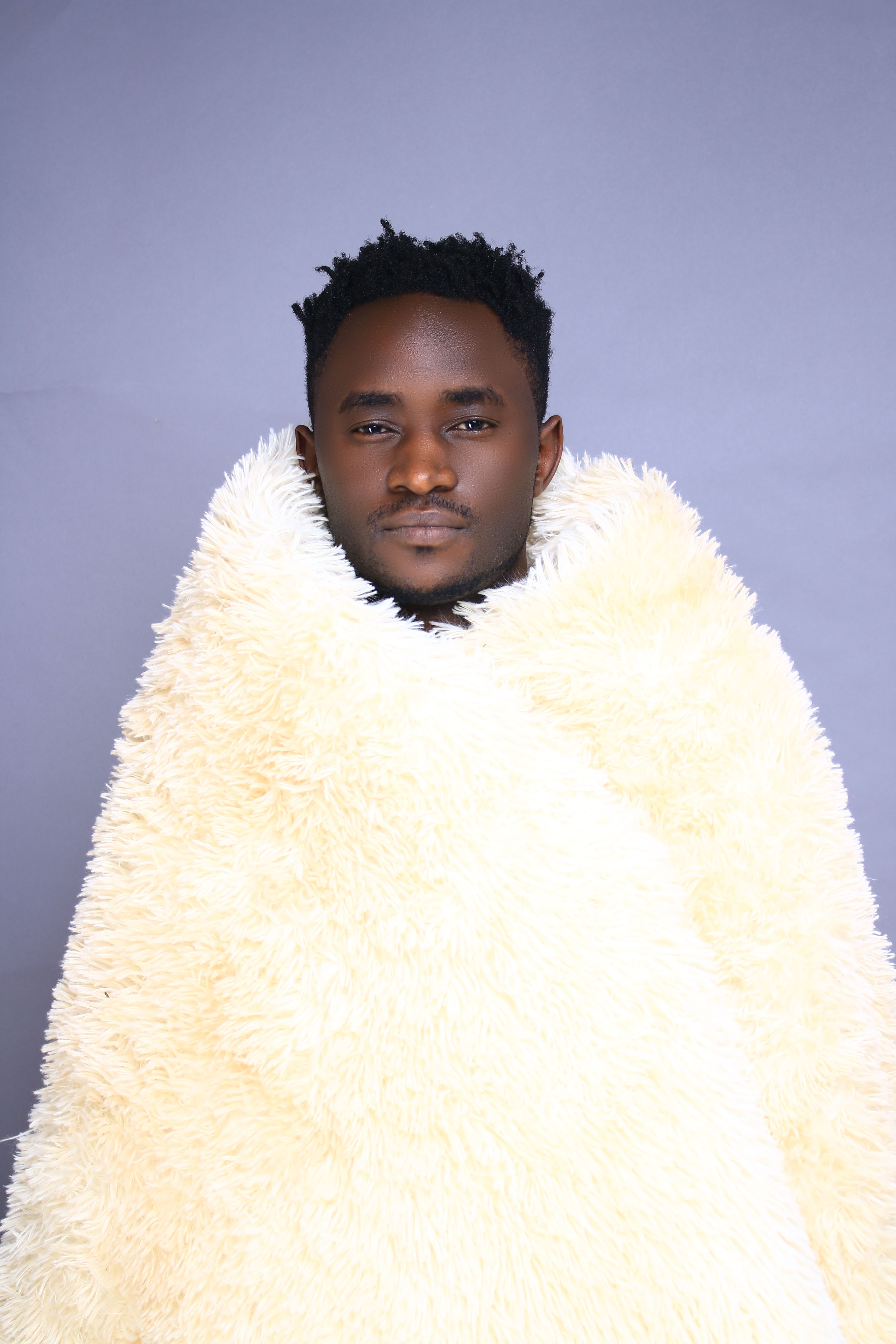 Young man warmly wrapped in a fluffy fur blanket, studio shot.