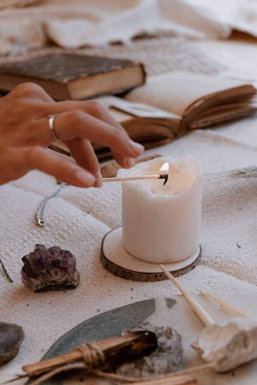 Free A hand lighting a candle with a matchstick, surrounded by books and crystals on a cozy setup. Stock Photo