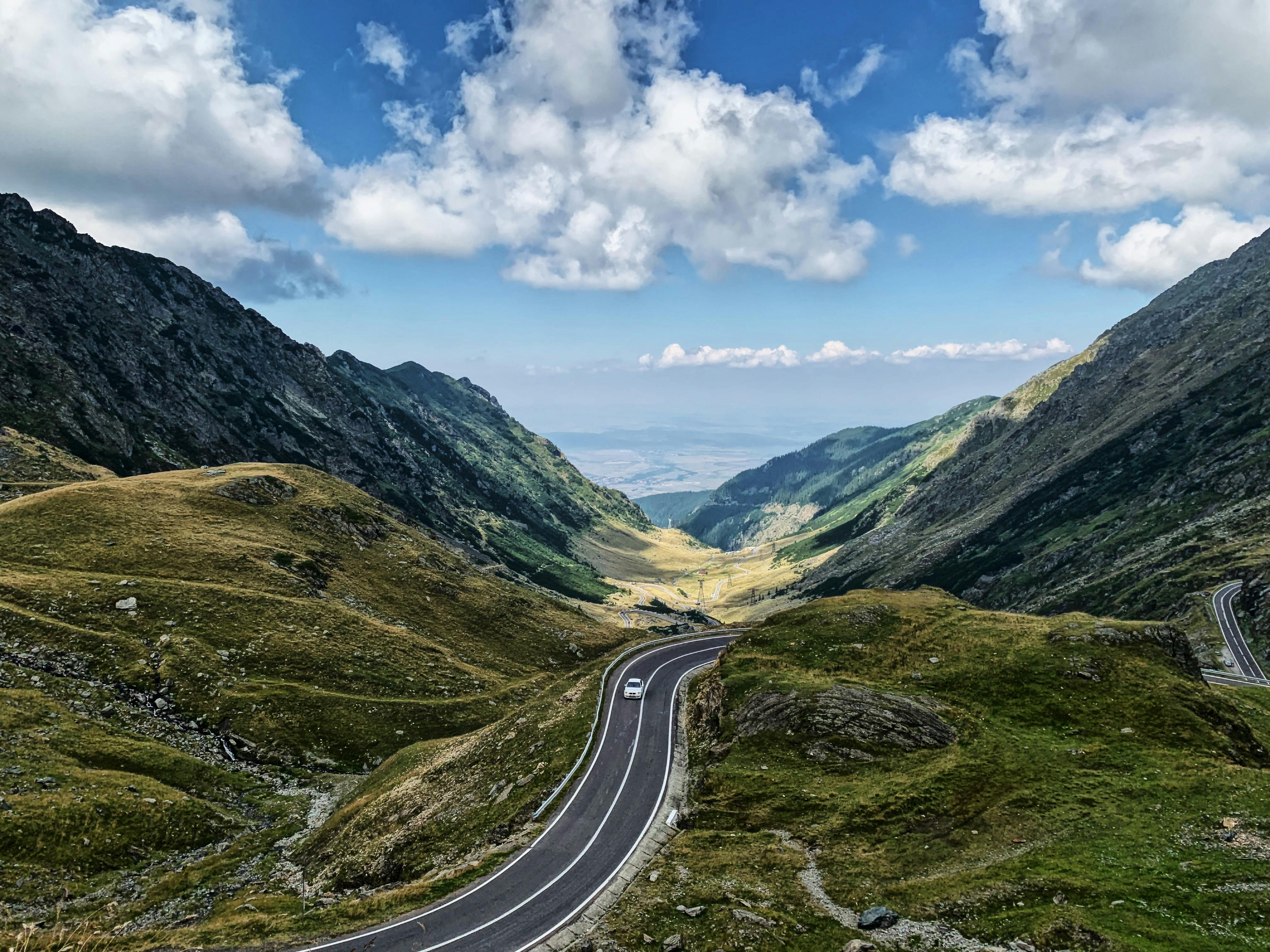 Breathtaking view of a winding mountain road under a blue sky filled with clouds.