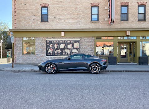 Luxury sports car parked on a city street in front of a brick building with large windows.