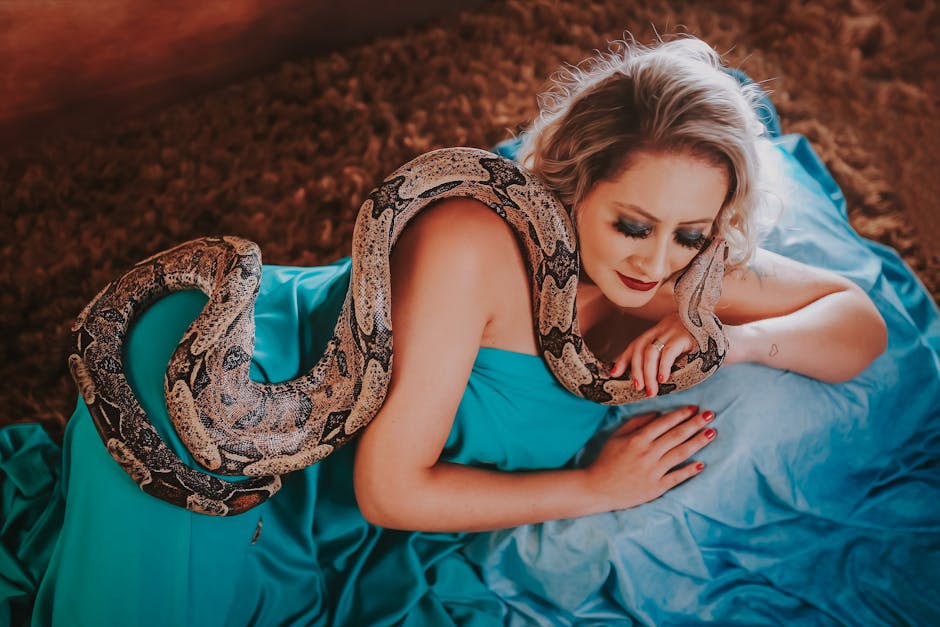 A woman elegantly posing indoors with a python on a blue dress.