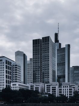 现代城市街道上，矗立着各种黑色和白色的当代建筑与摩天大楼，它们拥有玻璃外墙，映衬着阴云密布的天空