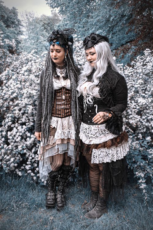 Free Two women in gothic attire standing amidst blossoms, exuding a mystical vibe. Stock Photo