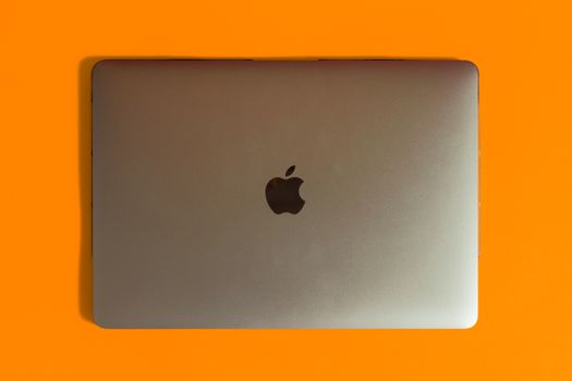 Silver laptop with iconic logo on a bright orange backdrop, showcasing minimalist design.