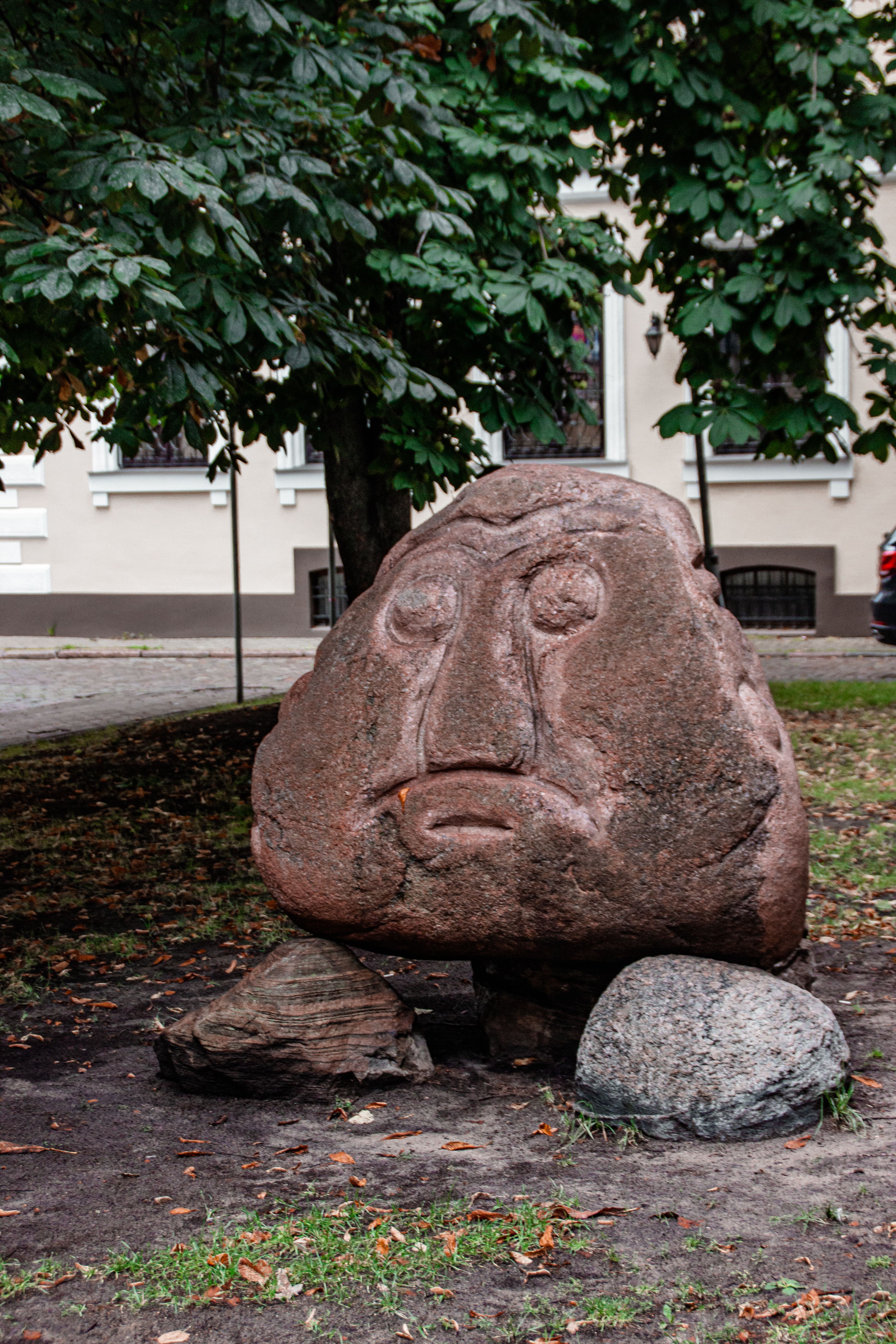 Artistic stone sculpture in a lush Riga park surrounded by greenery and trees.