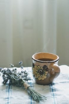 Brown ceramic cup of hot coffee with lavender bouquet on a checkered cloth.