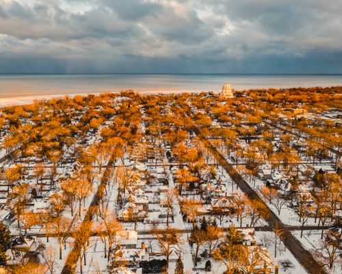 Free Aerial view of residential houses with roads and trees against sea shore under cloudy sky in fall Stock Photo