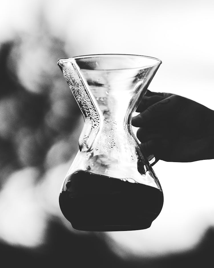 Hand Holding Clear Glass Pitcher With Black Liquid