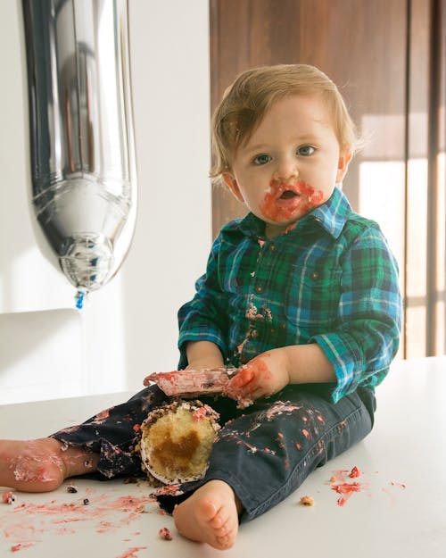 Free Cute Baby in Blue and Green Plaid Shirt Eating Bread with Icing Stock Photo
